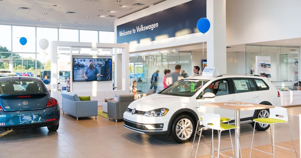 Inside the Wyatt Johnson Volkswagen dealership, customers and salespeople roaming the sales floor with Volkswagen models on display.